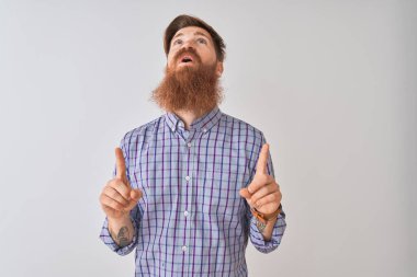 İzole edilmiş beyaz arka plan üzerinde duran genç, kızıl saçlı ve İrlandalı adam şaşırmış ve şaşırmıştı. Parmaklarıyla işaret ediyor ve kollarını kaldırıyordu..