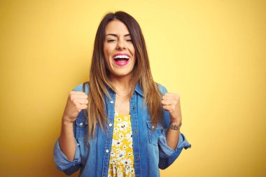 Sarı arka planda duran genç ve güzel bir kadın başarı için heyecanlı kolları havada ve gözleri kapalı zaferi kutlarken gülümsüyor. Kazanan konsept.