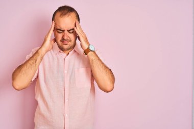 Soyutlanmış pembe arka planda duran zarif tişörtlü genç bir adam. Stres yüzünden başının üstünde baş ağrısı var. Migren ağrısı..