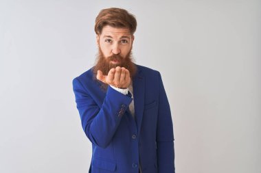 Genç, kızıl saçlı, takım elbiseli bir iş adamı, izole edilmiş beyaz arka planda dikilip kameraya bakıyor ve havada bir öpücük savuruyor. Güzel ve seksi. Aşk ifadesi.