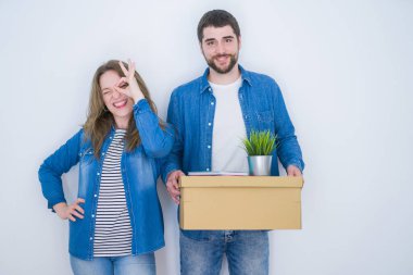 Genç çift, ellerinde karton kutuyla beyaz yalıtılmış arka planda yeni bir eve taşınıyor. Gülümsüyor, gülümsüyor. Elleri gözlerinde parmaklarından bakıyor.