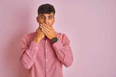 Soyutlanmış pembe arka planda duran zarif gömlekli genç Hintli adam yanlışlıkla ağızlarını kapatarak şok etti. Gizli konsept.