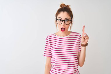 Kızıl saçlı, gözlüklü, çizgili tişörtlü ve atkuyruklu bir kadın izole edilmiş beyaz arka planda başarılı bir fikri işaret ediyor. Heyecanlı ve mutlu. Bir numara..