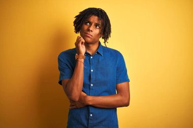 Rastgele kot gömlek giyen Afro bir adam izole edilmiş sarı arka planda duruyor, elleri çenesinde soru sormayı düşünüyor, düşünceli bir yüz ifadesi var. Düşünceli bir yüzle gülümsüyor. Şüphe kavramı.
