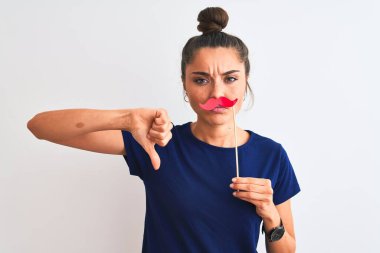 Genç, güzel bir kadın, izole edilmiş beyaz bir arka planda, popo partisi bıyığı tutuyor. Kızgın bir yüzü var. Negatif işaretler, baş parmakları aşağıda, reddedilme kavramı.