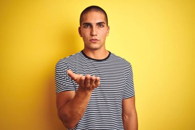 Sarı izole edilmiş arka plan üzerinde çizgili tişört giyen yakışıklı genç bir adam kameraya bakıp havada öpüşürken güzel ve seksi görünüyor. Aşk ifadesi.