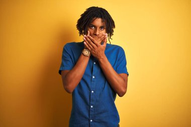 Rastgele kot gömlek giyen Afro bir adam izole edilmiş sarı arka planda dikiliyor ağzı yanlışlıkla ellerle kapatıyor. Gizli konsept.