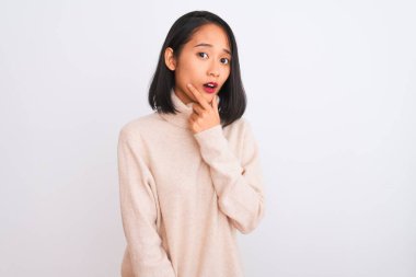 Balıkçı yaka kazak giyen genç bir kadın, izole edilmiş beyaz arka planda duruyor. İnançsızlığa, şaşkınlığa ve elleri çenesinde olan şaşkınlık ifadesine hayran görünüyor.