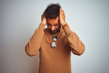 Zarif süveter ve güneş gözlüğü takan Hintli bir adam izole edilmiş beyaz arka planda duruyor. Ağrı ve migrenden dolayı baş ağrısı ve stresten muzdarip. Ellerini başının üstüne koy..