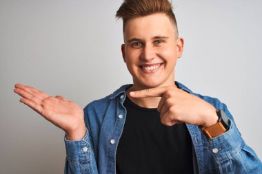 Soyutlanmış beyaz arka plan üzerinde duran kot gömlek giyen genç yakışıklı adam mutlu bir şekilde elini ve parmağını gösterdi.