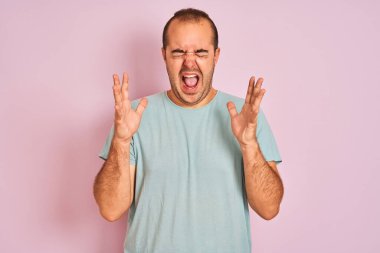 İzole edilmiş pembe arka planda duran mavi tişörtlü genç adam kollarını kaldırmış ve gözleri kapalı heyecanla haykırarak başarının çılgınlığını kutluyor. Kazanan konsept