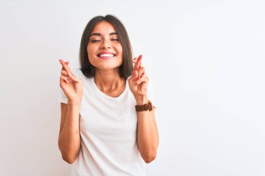 İzole edilmiş beyaz arka plan üzerinde sıradan tişörtler giyen genç ve güzel bir kadın umut ve gözlerin kapalı bir şekilde gülümseyerek el sallıyor. Şans ve batıl inanç..