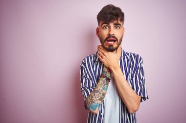 İzole edilmiş pembe arka planda duran çizgili tişörtlü genç adam bağırıyor ve boğuluyor çünkü acı verici bir boğulma. Sağlık problemi. Boğulma ve intihar konsepti.