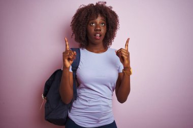 Sırt çantasıyla gezen Afrikalı genç Afrikalı turist kadın pembe arka planda şaşkın şaşkın bakıyor ve parmaklarıyla işaret ediyor ve kollarını kaldırıyordu..