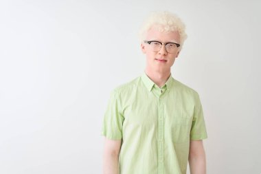 Yeşil tişörtlü ve gözlüklü genç albino sarışın adam izole edilmiş beyaz arka plan ve yüzünde ciddi bir ifade var. Basit ve doğal bir şekilde kameraya bakıyorsun..