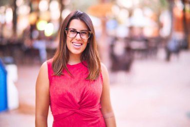 Genç ve güzel bir kız gülümseyerek mutlu ve kendinden emin bir şekilde parkta yürüyor, yüzünde bir gülümsemeyle duruyor.