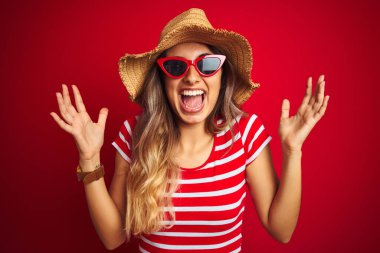 Kırmızı arka plan üzerinde güneş gözlüğü ve yaz şapkası takan genç ve güzel bir kadın kolları havada ve gözleri kapalı heyecanla haykırarak başarının çılgınlığını kutluyor. Kazanan konsept