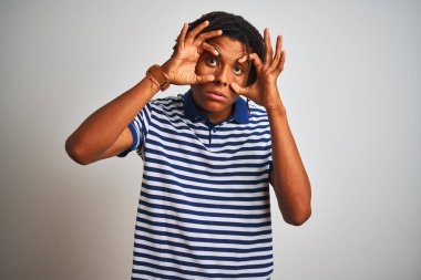 Sarı çizgili mavi polo giyen Afro bir adam izole edilmiş beyaz arka planda duruyor parmaklarıyla gözlerini açmaya çalışıyor, uykulu ve yorgun bir şekilde sabah yorgunluğu çekiyor.