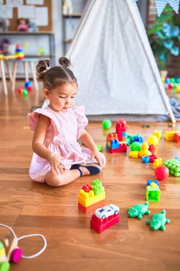Genç ve güzel bir çocuk yerde oturmuş kreşteki yapı taşlarıyla oynuyor.