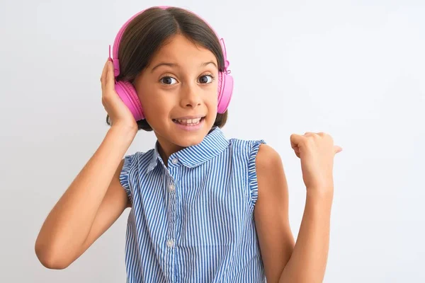 美しい子供の女の子は 孤立した白い背景の上にヘッドフォンを使用して音楽を聴くと幸せな顔の笑顔で親指で横に示す — ストック写真