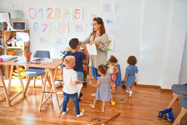 Beautiful teacher and group of toddlers playing around lots of toys at kindergarten