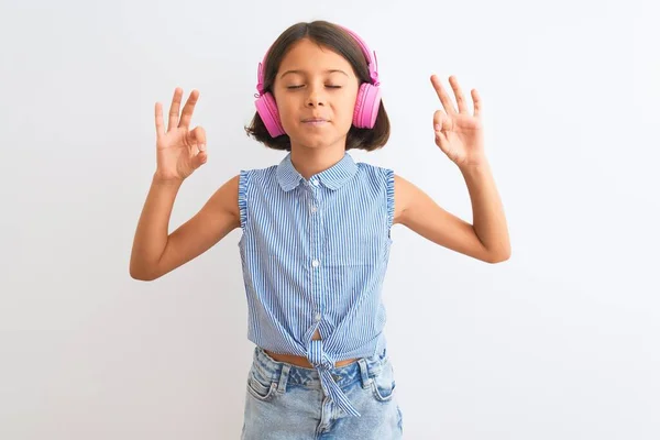 美丽的小女孩在孤立的白色背景下 用耳机听音乐 闭上双眼微笑 用手指做冥想手势 瑜伽概念 — 图库照片