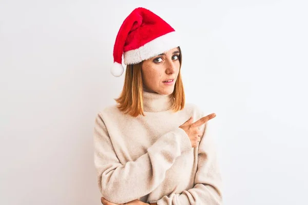 美しい赤毛の女性は孤立した背景の上にクリスマスの帽子を身に着けています広告 深刻かつ穏やかな顔を示す側に手指で指して — ストック写真