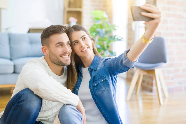 Ungt par sitter på golvet i nya hus med en selfie p — Stockfoto