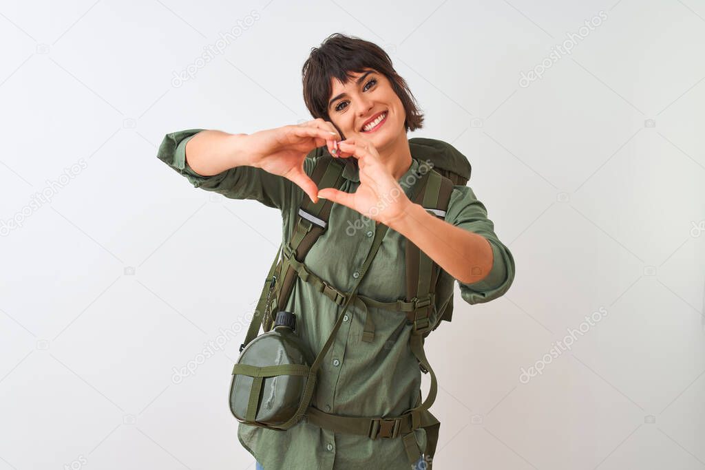 Beautiful hiker woman wearing backpack and water canteen over isolated white background smiling in love showing heart symbol and shape with hands. Romantic concept.