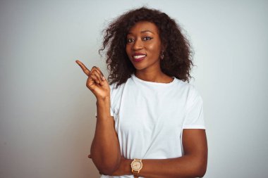 Genç Afro-Amerikalı kadın tişört giyiyordu. İzole edilmiş beyaz arka planda duruyordu. Yüzünde kocaman bir gülümseme vardı..