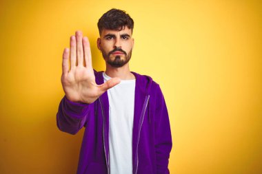 İzole edilmiş sarı arka plan üzerine spor mor kazak giyen genç adam avucunun içi gibi şarkı söylemeyi kesiyor. Yüzünde olumsuz ve ciddi bir jest olan uyarı ifadesi.