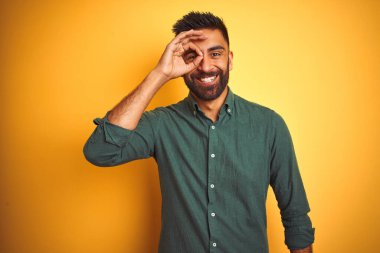 Genç hintli işadamı izole beyaz arka plan üzerinde duran zarif gömlek giyen el gülümseyerek ok jest yapıyor, mutlu yüz ile parmaklarından bakan göz.