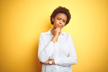Afrika kökenli Amerikalı iş kadını, izole edilmiş sarı arka planda, elleri çenesinde sorguda, düşünceli bir ifade takınıyor. Düşünceli bir yüzle gülümsüyor. Şüphe kavramı.