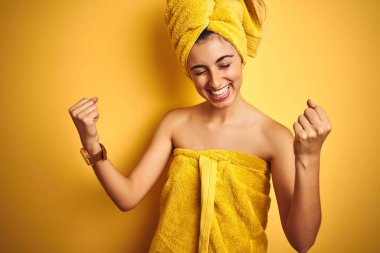 Sarıya boyanmış arka planda duş havlusu takan genç ve güzel bir kadın çok mutlu ve heyecanlı bir şekilde kollarını kaldırıp, gülümseyerek ve başarı çığlıkları atarak zafer jesti yapıyor. Kutlama konsepti.