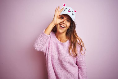 Genç, güzel bir kadın pembe kepli arka planda dikiliyor. El hareketleriyle gülümsüyor, gözleriyle mutlu yüzüyle parmaklarının arasından bakıyor..