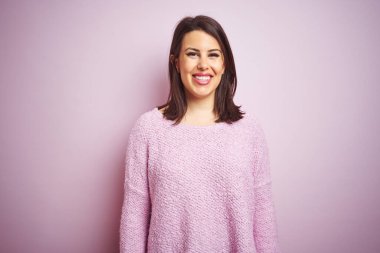 Genç, güzel esmer bir kadın pembe izole bir arka plan üzerine kazak giyiyor ve yüzünde mutlu ve havalı bir gülümseme var. Şanslı kişi..