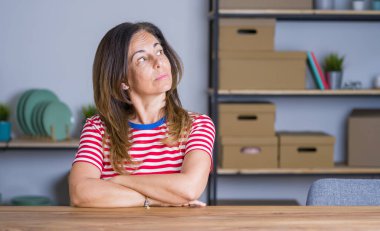 Orta yaş yaşlı kadın evde masada oturan kolları ile yan bakarak ikna ve kendinden emin geçti