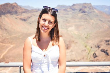 Genç ve güzel bir turist kadın dağ manzarasında mutlu bir şekilde gülümsüyor yaz tatilinin tadını çıkarıyor.