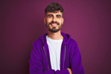 İzole edilmiş sarı arka planda duran çizgili polo giyen genç adam kollarını kavuşturup kameraya bakarken gülümsüyor. Pozitif kişi.