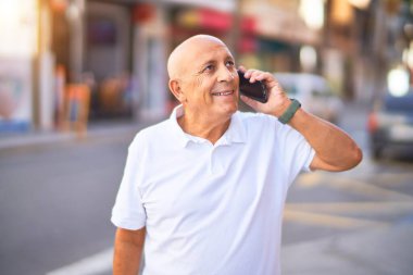 Kıdemli yakışıklı adam mutlu ve kendinden emin gülümsüyor. Yüzünde gülümsemeyle kasaba caddesinde telefonla konuşuyor.