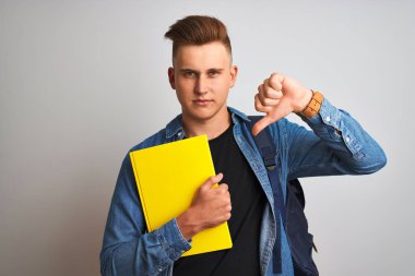 İzole edilmiş beyaz arka plan üzerinde kot gömlek giyen genç öğrenci not defteri, kızgın yüz, olumsuz işaret baş parmaklar aşağı, reddedilme konsepti