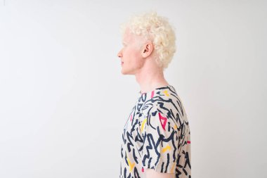 Renkli tişört giyen genç albino bir adam izole edilmiş beyaz arka plan üzerinde duruyor. Yan tarafa bakıyor, rahat bir poz veriyor kendine güvenen bir gülümsemeyle doğal bir yüz ifadesi sergiliyor..