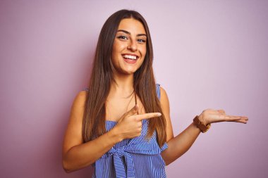 İzole edilmiş pembe arka planda duran çizgili elbiseler giyen genç ve güzel bir kadın hayrete düşmüş ve kameraya gülümserken eliyle ve parmağıyla işaret ediyordu..