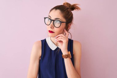 Saçlı, atkuyruklu, zarif bir elbise ve gözlüklü, pembe bir arka planı olan, elleri çenesinde soru soran, düşünceli bir kadın. Düşünceli bir yüzle gülümsüyor. Şüphe kavramı.