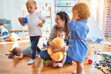 Güzel öğretmen ve bir grup çocuk anaokulunda bir sürü oyuncakla oynuyorlar.