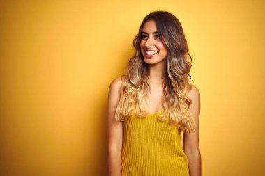 Sarı arka plan üzerine tişört giyen güzel bir kadın yüzünde gülümseme, doğal bir ifade ile bir o yana bir bu yana bakıyor. Kendinden emin gülen.