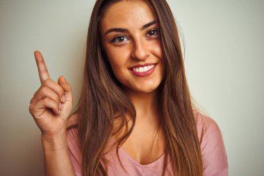 İzole edilmiş beyaz arka plan üzerinde duran pembe tişört giyen genç ve güzel bir kadın bir fikir ya da soru işareti ile şaşırdı.