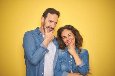 Güzel bir orta yaşlı çift, izole edilmiş sarı arka planda kot tişört giyip kollarını kavuşturmuş ve çenesini kaldırmış bir şekilde kameraya bakıp gülümsüyorlar. Olumlu düşünüyorum..
