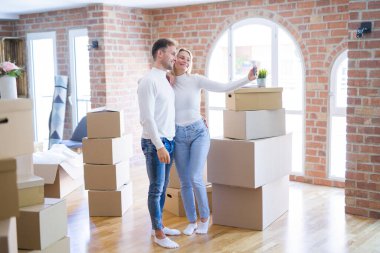 Karton kutular etrafında yeni evde selfie çekmek için akıllı telefon kullanarak ayakta genç güzel çift