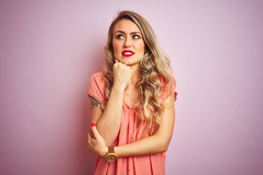 Pembe izole edilmiş arka planda duran tişört giyen genç ve güzel bir kadın bir soru hakkında endişeli ve gergin bir şekilde düşünüyor.